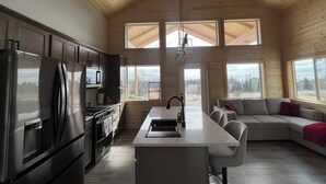 Une cuisine moderne dotée d’un îlot central, d’appareils électroménagers en acier inoxydable et de grandes fenêtres offrant une vue sur l’extérieur.