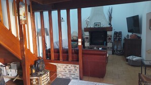 A cozy living room with a fireplace, wooden beams, a sofa, and a television. - House sleeps 6, parking, daily rental, 10 mmde rouen, 1 hde paris (Criquebeuf-sur-Seine)