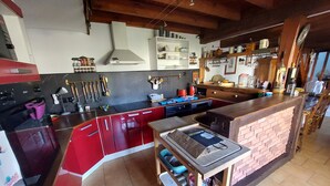 A modern kitchen with red cabinets, a central island, and a brick accent wall. - House sleeps 6, parking, daily rental, 10 mmde rouen, 1 hde paris (Criquebeuf-sur-Seine)