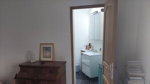 A room with a wooden dresser, a framed picture, a small bottle, a mirror, a sink, and a door leading to another room. - House sleeps 6, parking, daily rental, 10 mmde rouen, 1 hde paris (Criquebeuf-sur-Seine)