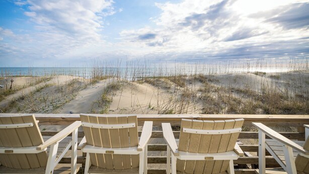Blick auf einen Strand mit Holzstühlen und einer Holzterrasse.