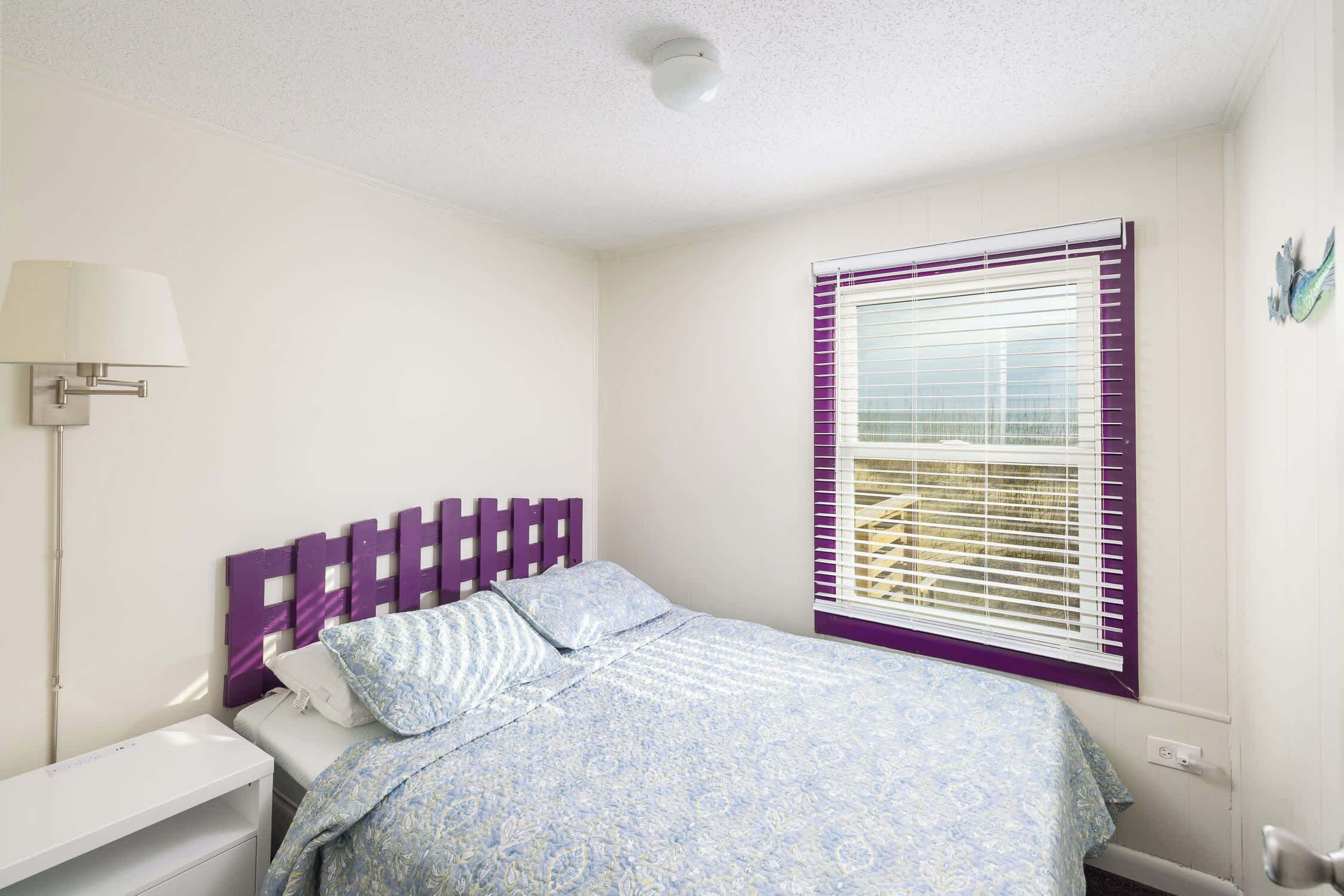 A bedroom with a bed, a nightstand, a lamp, and a window with blinds.