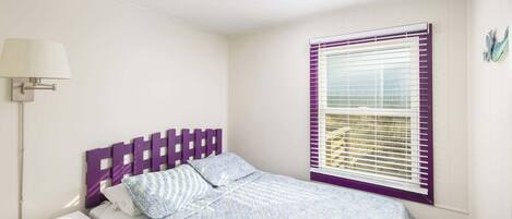 A bedroom with a bed, a nightstand, a lamp, and a window with blinds.