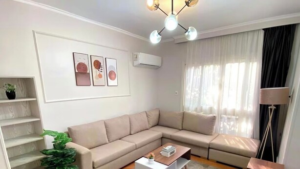 Ein modernes Wohnzimmer mit einem Ecksofa, einem Couchtisch, einem grauen Teppich, einer Treppe und einer Topfpflanze.
