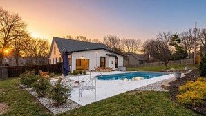 A house with a swimming pool, a patio with chairs, and a fenced yard.