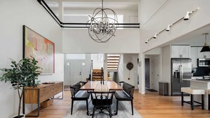 A modern dining area with a wooden table, black chairs, a chandelier, and a potted plant.