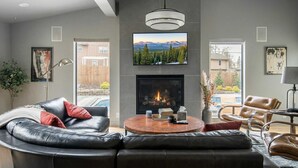 A modern living room with a fireplace, leather sofa, and a large TV mounted above it.