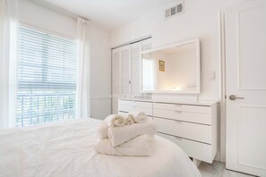 Ein Schlafzimmer mit einem Bett, einem Schminktisch, einem Spiegel und einem Fenster mit Jalousien.