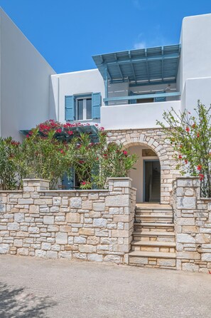 A modern building with a stone wall, a covered entrance, and a staircase leading to the door. - Alyki Maisonette by the beach (Alyki)