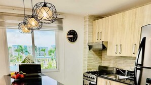 Een keuken met een centraal eiland, houten kasten, roestvrijstalen apparatuur en hangende lampen.