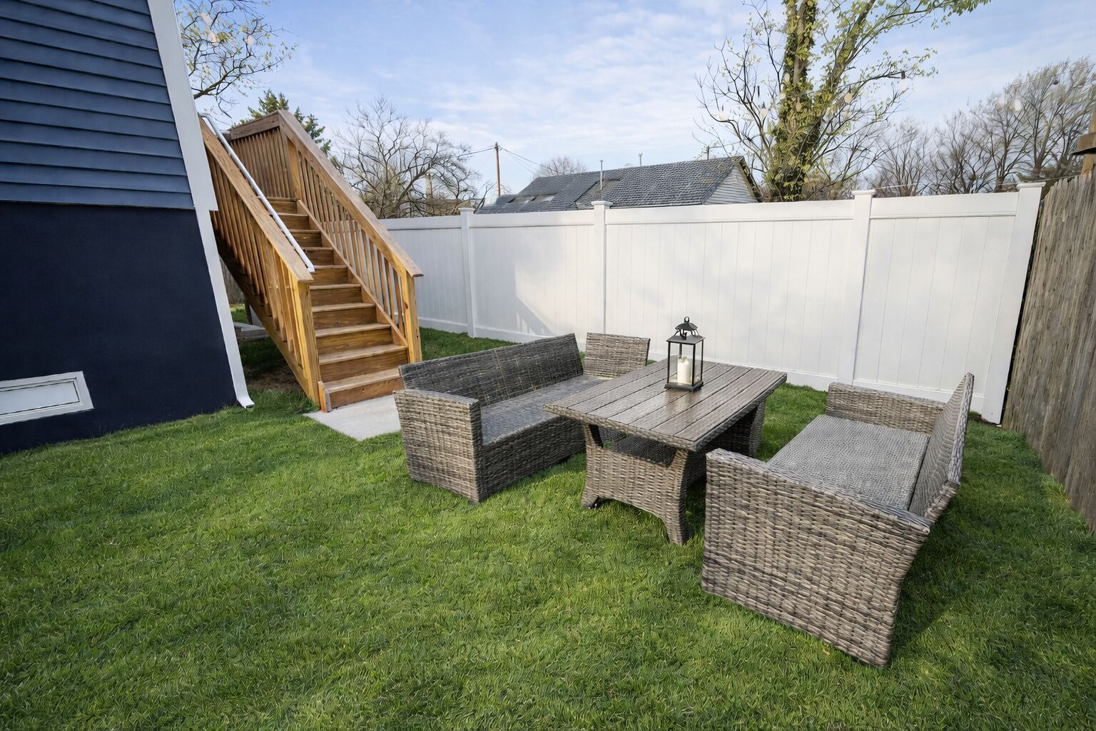 Ein Garten mit einer Holztreppe, einem weißen Zaun und einer Sitzgruppe aus Rattan mit Tisch und Stühlen.