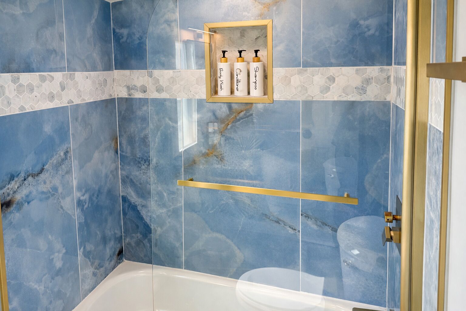 A bathroom with blue marble tiles, a framed shelf with toiletries, and a gold-framed shower door.