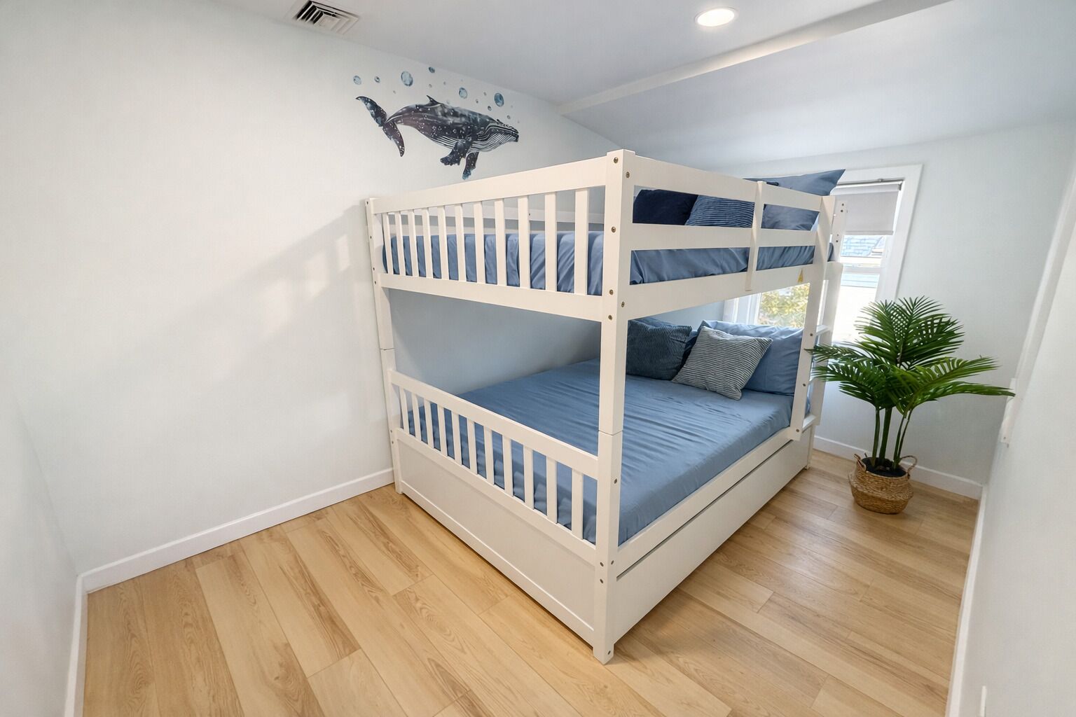 A bunk bed with three levels, a potted plant, and a wall decal of a whale.