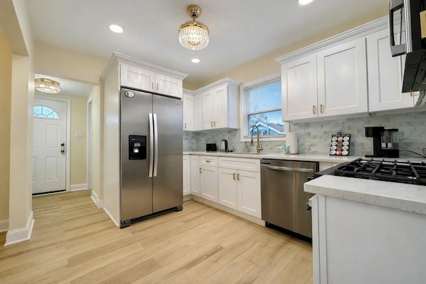 A modern kitchen with white cabinets, stainless steel appliances, and a wooden floor.