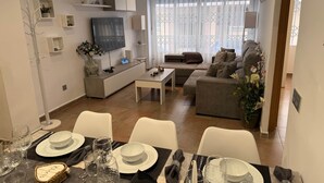 Ein modernes Wohnzimmer mit Sofa, Fernseher und Essbereich, vorbereitet für eine Mahlzeit.