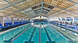 Une piscine intérieure avec des couloirs bien délimités, des chaises longues bleues et un plafond haut doté de lucarnes.