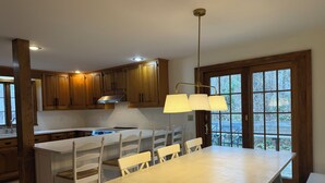 Une cuisine moderne avec des meubles en bois, un îlot central doté de chaises, une grande fenêtre offrant une belle vue et des luminaires suspendus.