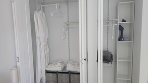 En garderobe med ophængte badekåber, foldede håndklæder og åbne hylder.