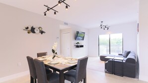 Et moderne spiseområde med et bord dækket til fire personer, en sofa og et TV ophængt på væggen.