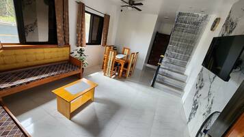 A living room with a sofa, coffee table, dining table, chairs, and a TV.