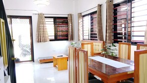 A dining area with a wooden table and chairs, a small side table, and a window with curtains.