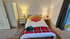 Une chambre à coucher avec un lit, deux tables de chevet avec des lampes, une fenêtre avec des rideaux, une porte et un sol recouvert d’une moquette.