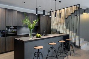 A modern kitchen with dark wood cabinets, a central island with stools, pendant lighting, and a decorative wall panel. - Luxury Villa Viktor Tireli for up to 14 guests by Istrabook (Krsan)