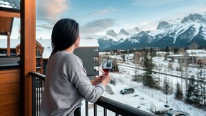 A person holding a glass of red wine on a balcony with a mountain view. - Timberline Hydeaway at Ascent (Canmore)