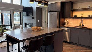 A modern kitchen with a large island, bar stools, a built-in oven, and a coffee machine. - Timberline Hydeaway at Ascent (Canmore)
