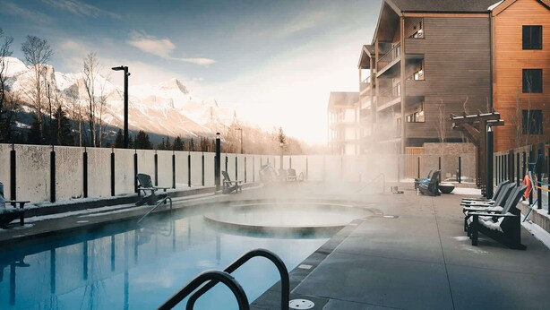 A pool area with lounge chairs, a hot tub, and a building with balconies. - Timberline Hydeaway at Ascent (Canmore)