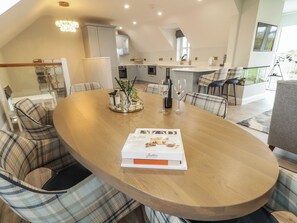 A modern kitchen with white cabinets, a dining area with plaid chairs, and a table with a magazine and wine glasses. - PORTNABLAGH COTTAGE, family friendly in Portnablagh, County Donegal (Dunfanaghy)