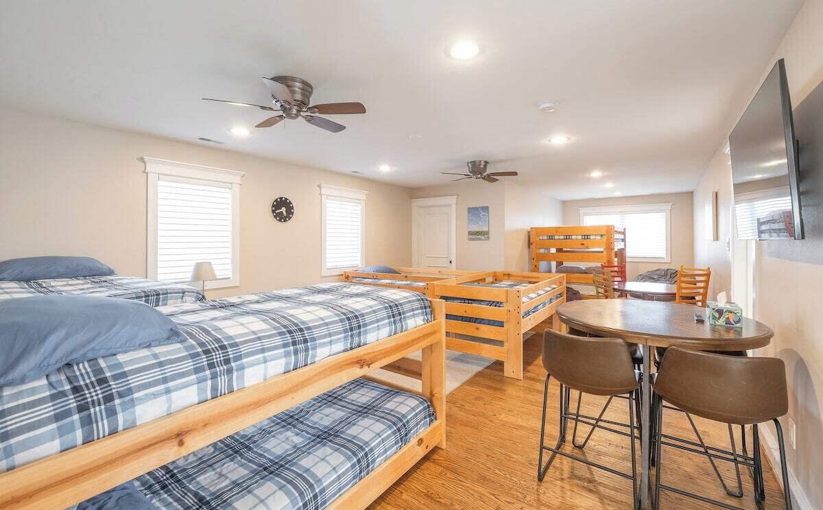 Une chambre de dortoir équipée de lits superposés, d’une table à manger, de chaises, de ventilateurs de plafond et d’un téléviseur.