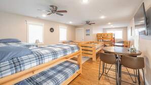 A dormitory room with bunk beds, a dining table, chairs, ceiling fans, and a TV. - Honeysuckle House (Gravois Mills)