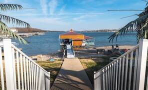Un muelle frente al agua con una estructura de madera, un sendero de concreto que lleva a él y una vista despejada del agua.