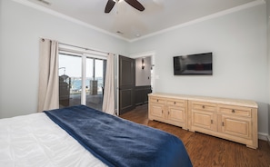 Un dormitorio con cama, televisor, cómoda de madera y puerta corrediza de vidrio que da a un balcón.