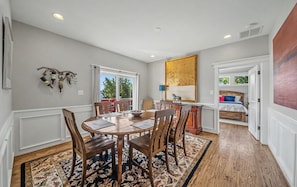 Un coin repas avec une table et des chaises en bois, un tapis à motifs et une vue sur l’extérieur par une fenêtre.