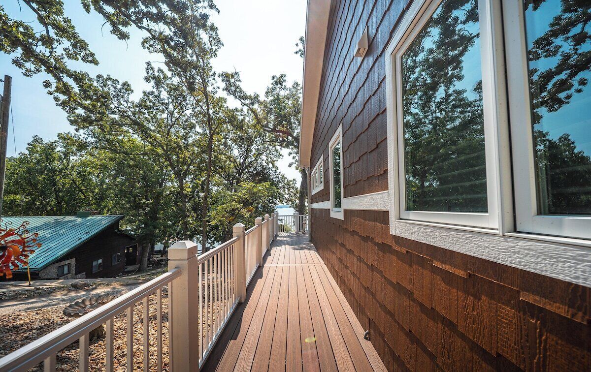 Une terrasse en bois dotée d’une rambarde, qui mène à un bâtiment aux grandes fenêtres offrant une vue sur les arbres.