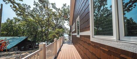 Una terraza de madera con barandilla que conduce a un edificio con ventanas amplias y vistas a árboles.