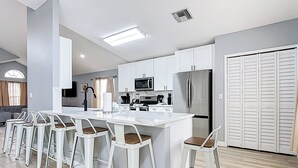 Una cocina moderna con armarios blancos, un refrigerador de acero inoxidable, una isla central con taburetes de bar y un microondas.