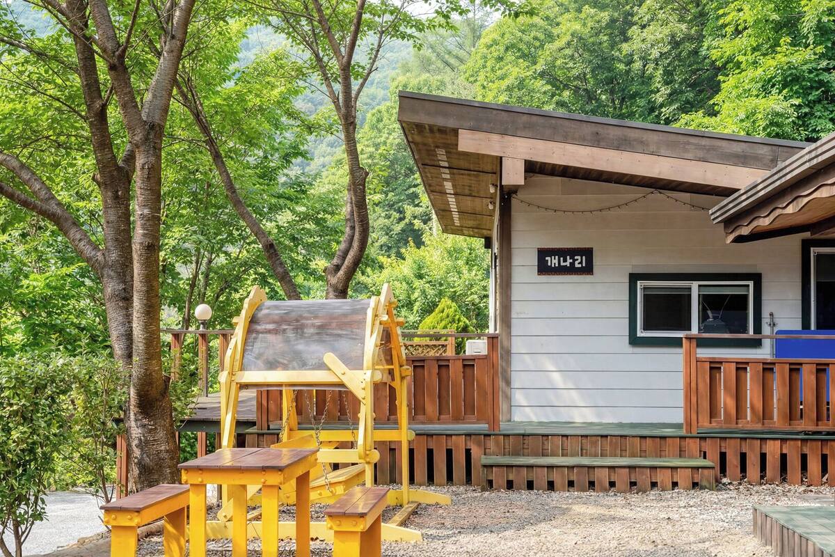 A wooden cabin with a deck, a swing set, and a window with a sign.