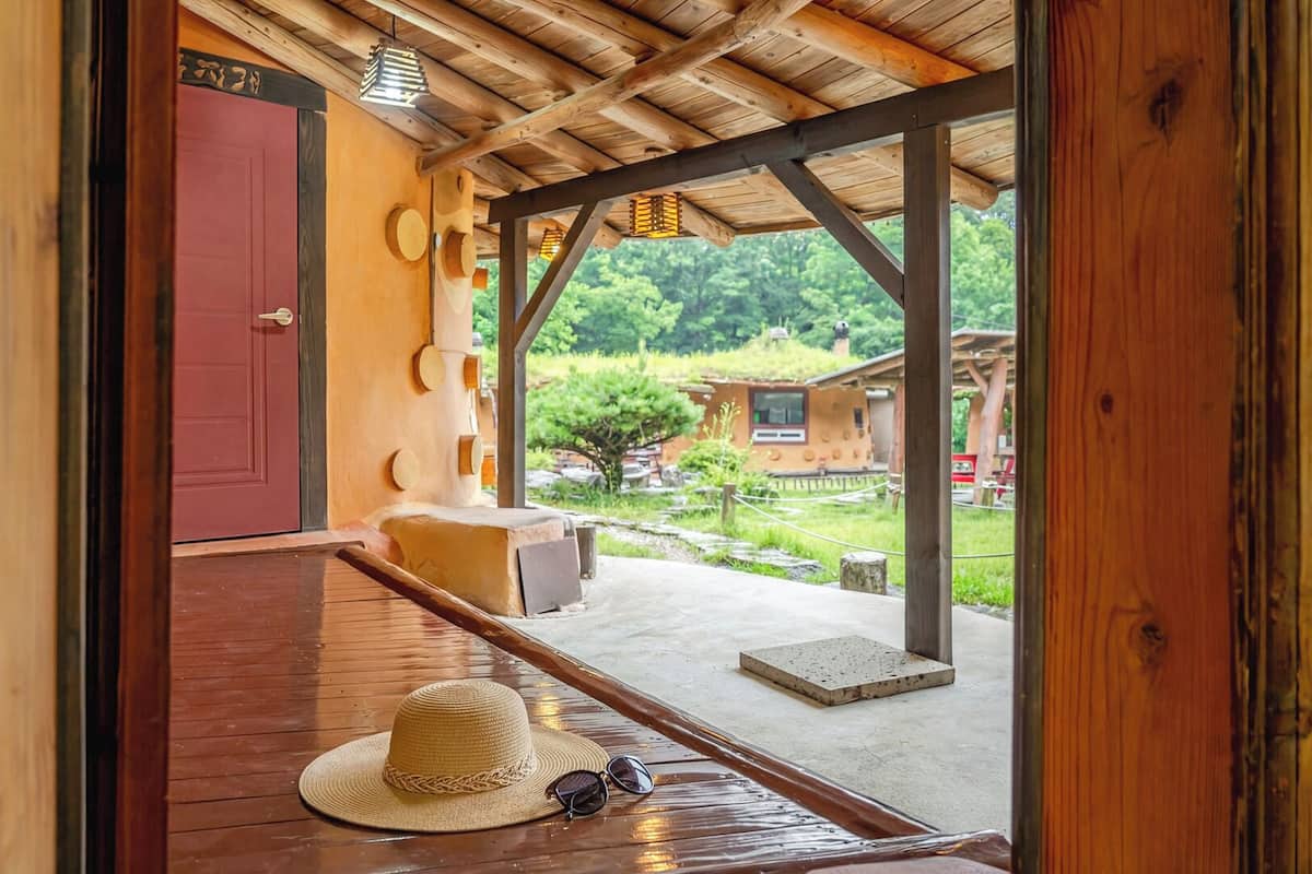 A wooden porch with a red door, a hat, and sunglasses on the floor.
