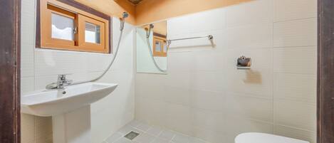 Un baño con lavamanos, inodoro, ducha y toallero.