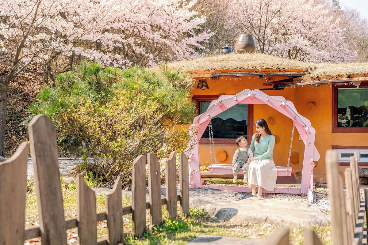 A wooden structure with a thatched roof, a pink swing, and a bench.