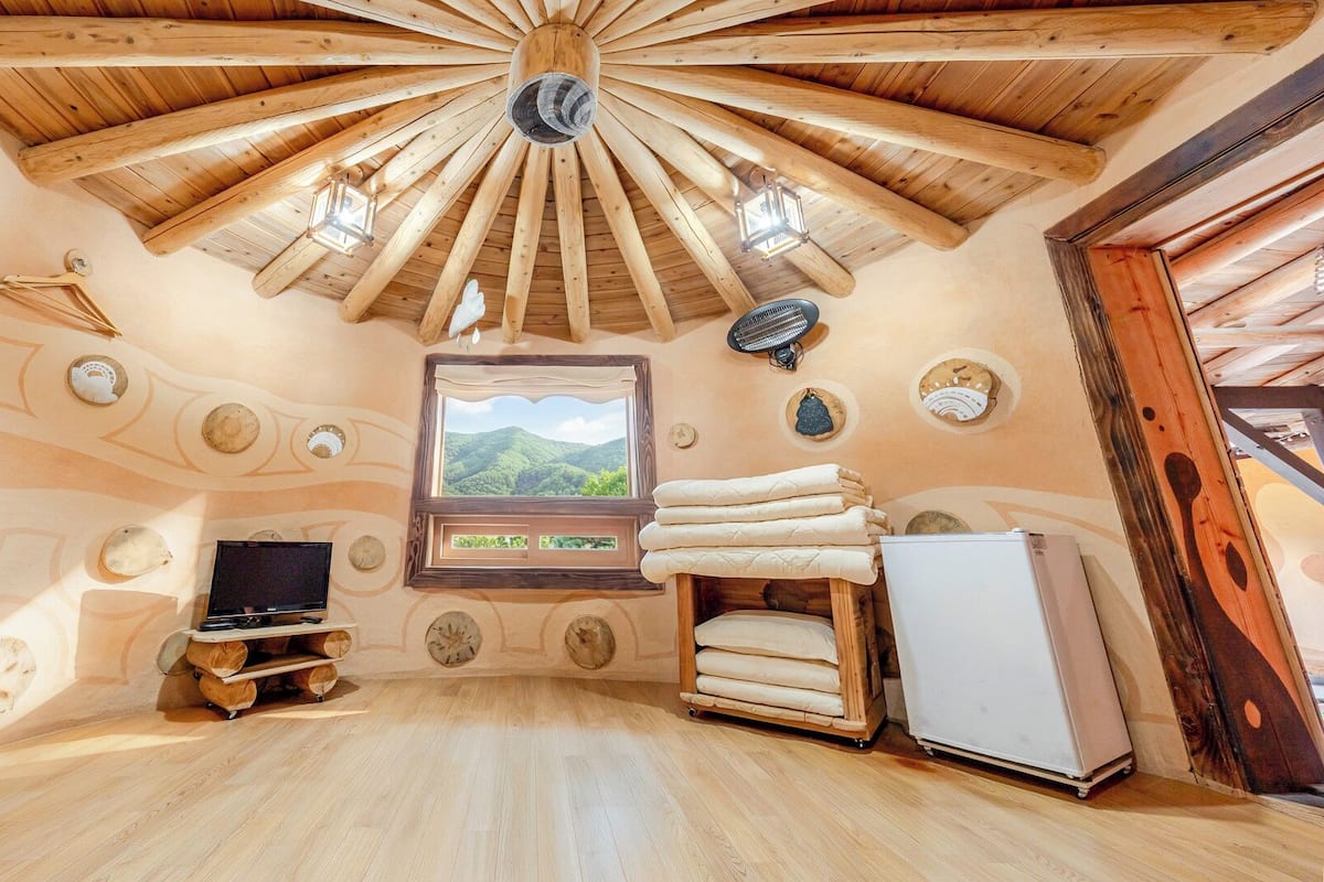 A rustic room with a wooden ceiling, a television, a window with a mountain view, and a refrigerator.