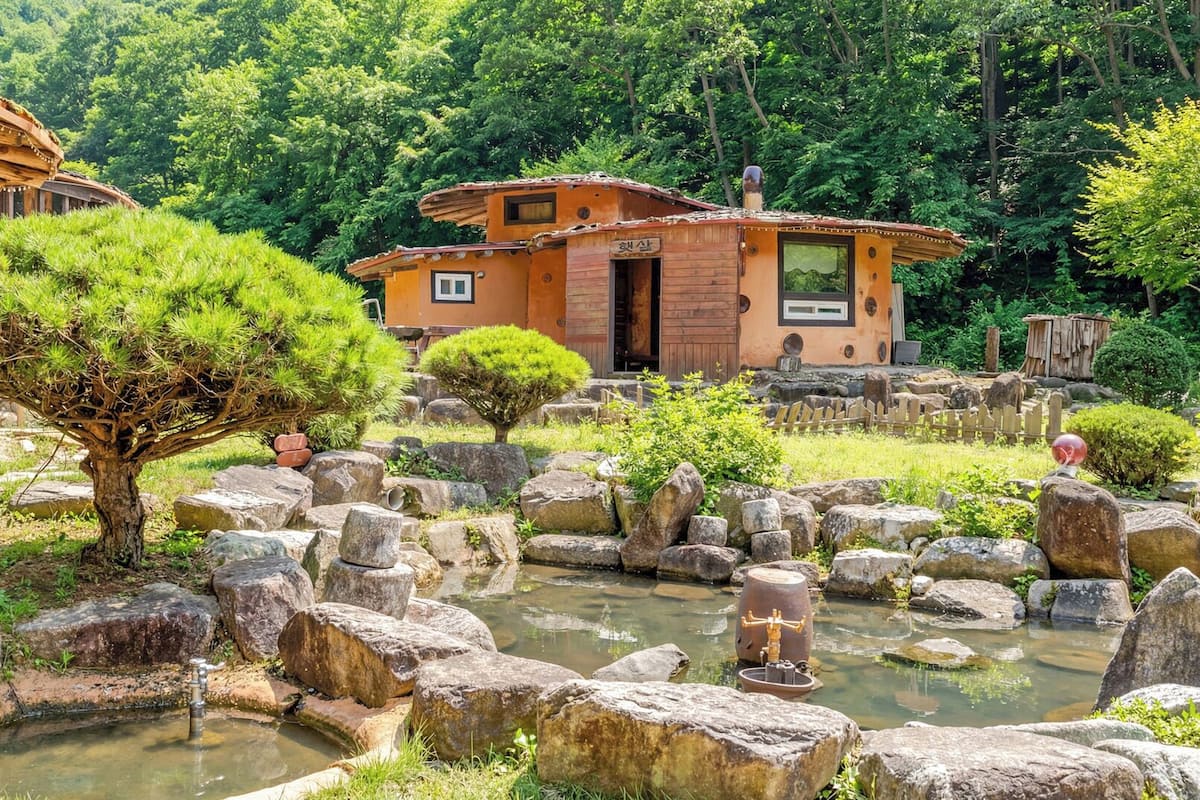A traditional Japanese-style building with a garden featuring a pond, rocks, and bonsai trees.