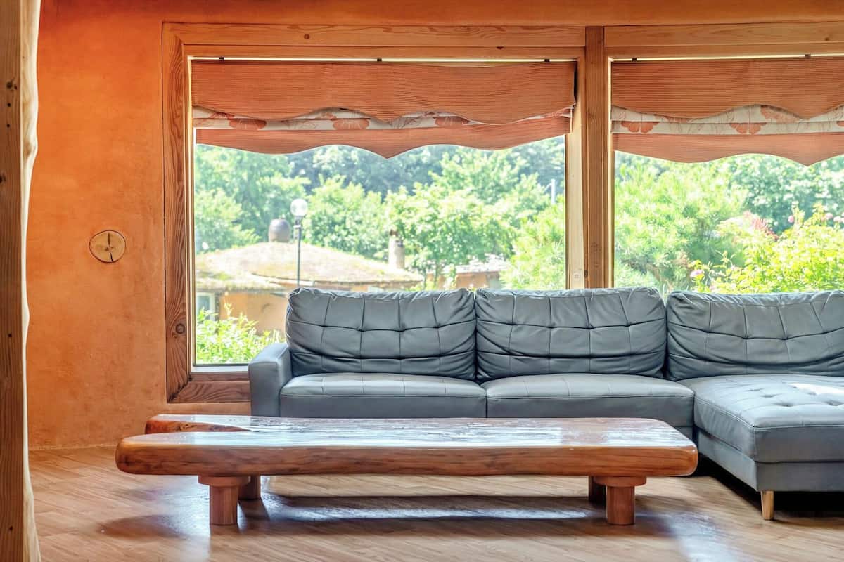 A modern living room with a sectional sofa, a wooden coffee table, and large windows offering a view of greenery.