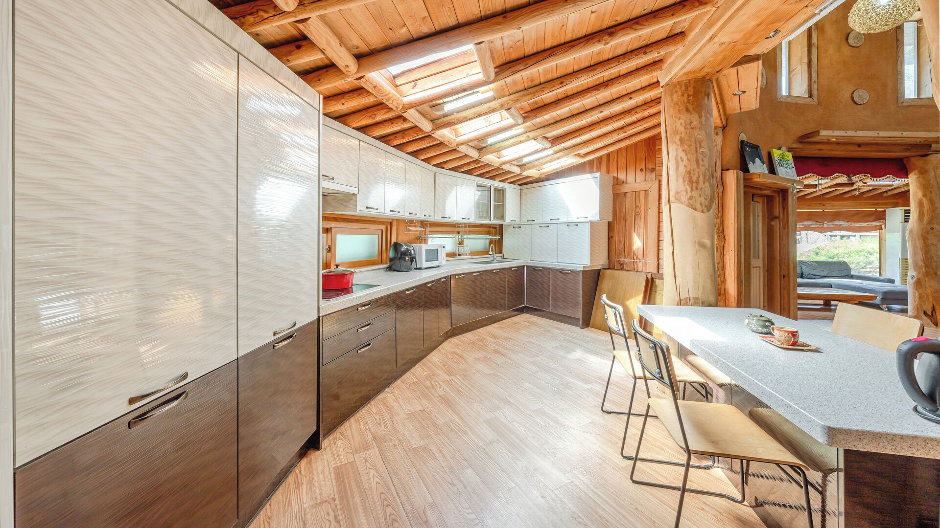Una cocina moderna con vigas de madera, un comedor con sillas y vistas al exterior.