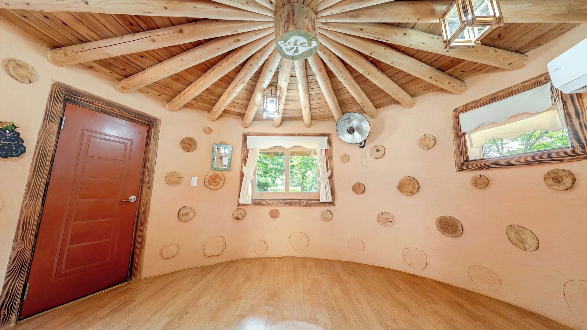 A room with a wooden ceiling, a wooden door, a window with curtains, and a mirror on the wall.