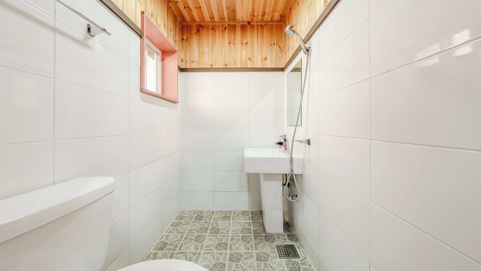 A small, tiled bathroom with a wooden ceiling, a white sink, and a toilet.