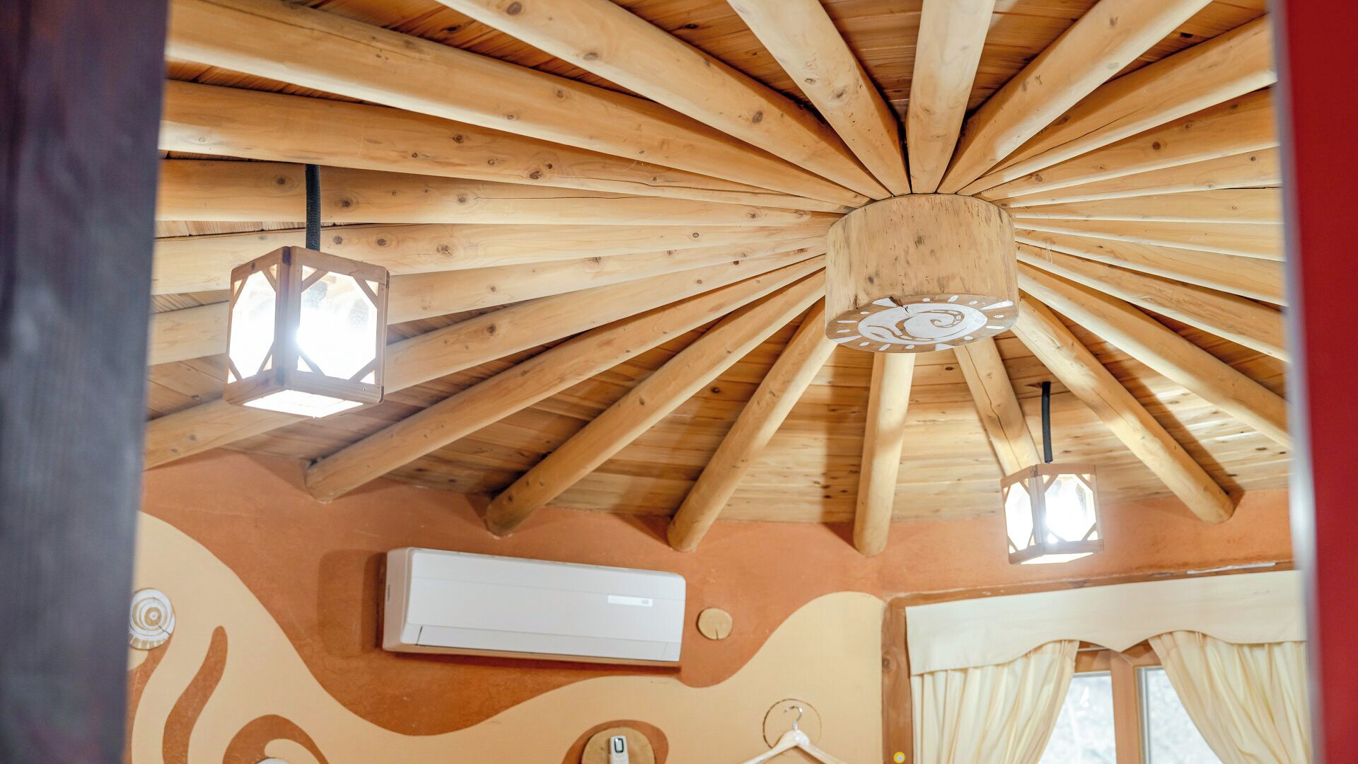 A room with a wooden ceiling, a central light fixture, and an air conditioning unit.